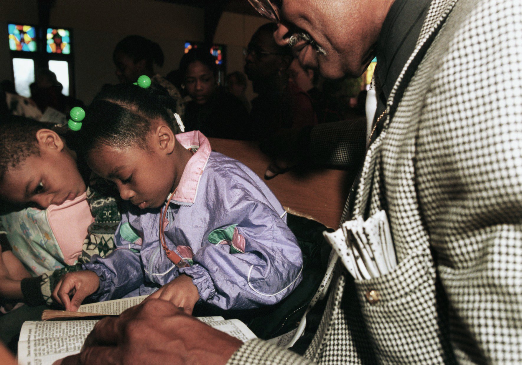 While their mother sings in the choir, Leon Hall, right, keeps a watchful eye on Eshawn, 7, and Cambria Allen, 6, as they try to follow along with the congregation's reading of passages from the Bible during Sunday's service on March 12, 2000. The church received a \$5,000 donation to be put toward children and combatting violence, in the wake of Kayla Rolland's life being taken by a fellow first grader, February 29, at nearby Buell Elementary School. (Flint Journal File Photo by Melissa Lyttle)