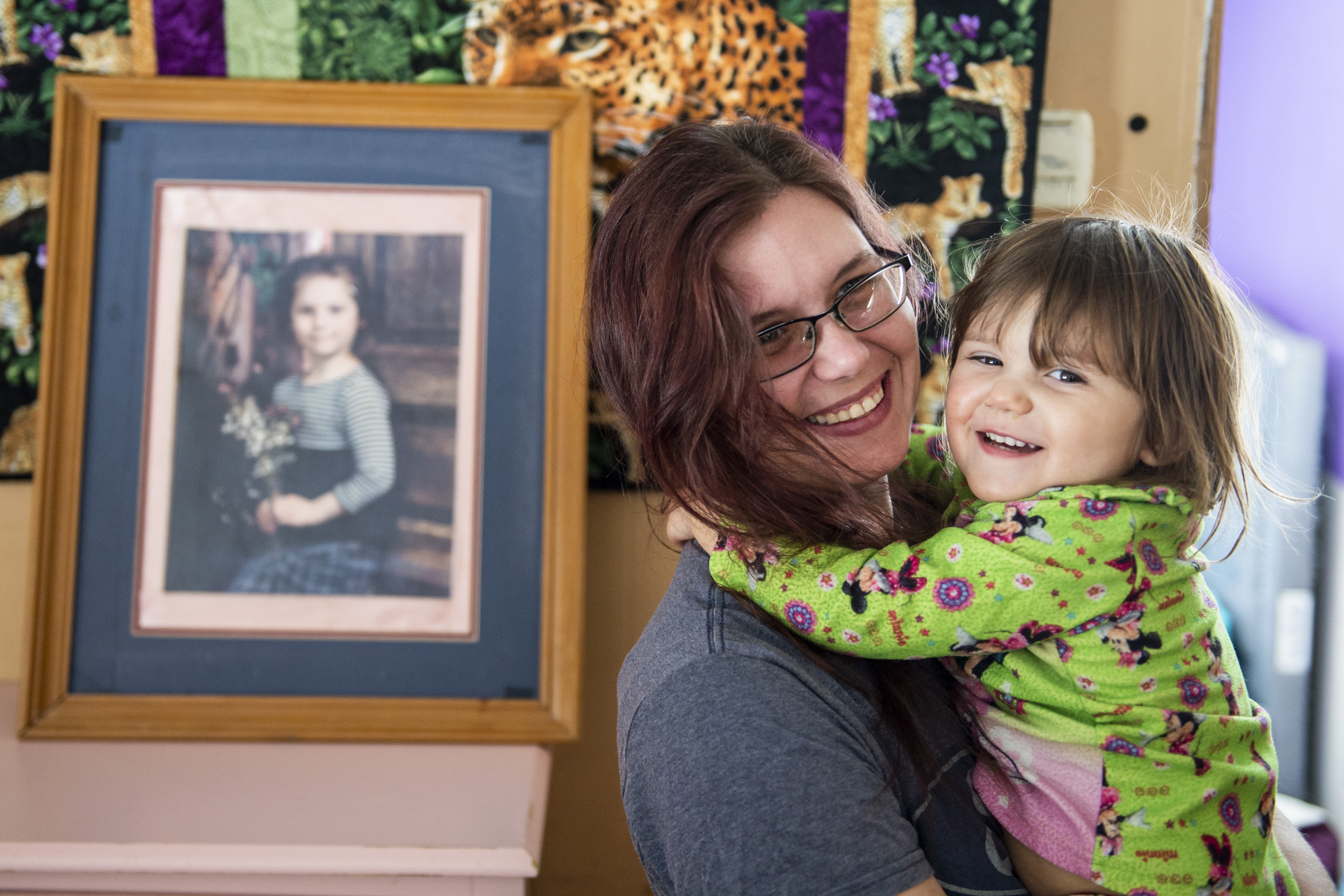 Elizabeth Krasinski and her daughter Savannah Krasinski, 2, pose for a photograph in Tawas City on Thursday, Feb. 20, 2020. Elizabeth lost her sister, Kayla Rolland (pictured in the frame), 20 years ago in a school shooting when Rolland was only in first grade. In 2000, the story made national news as Rolland is amongst the youngest of school shooting victims.