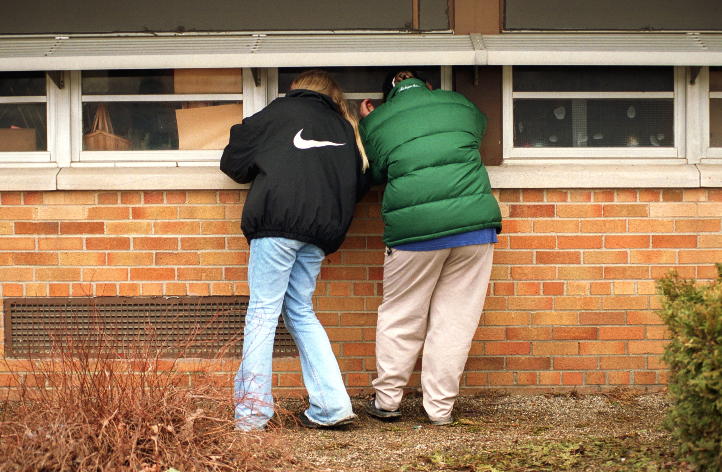 With a morbid curiosity, Katrina Bailey, 13, left, and Cassandra French, 14, peer into classroom windows at Buell Elementary School in hopes of seeing where the shooting of Kayla Rolland, 6, occurred on March 1, 2000. "I'm just trying to visualize what happened so I can understand why it happened," said Bailey. Both girls attended Buell when they were younger. (Flint Journal File Photo by Melissa Lyttle)